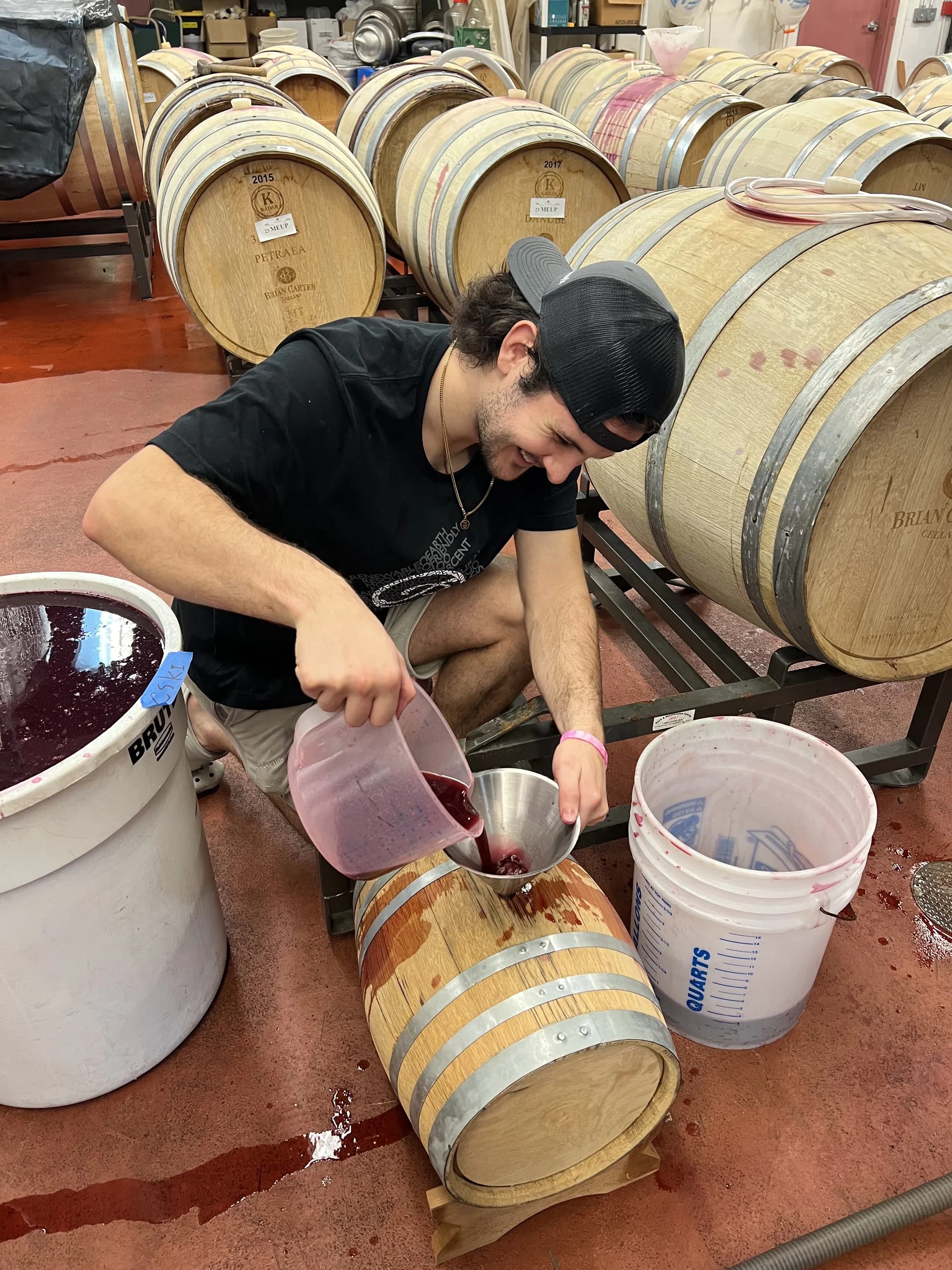 A cellar hand filling an oak barrel with young red wine in the Brian Carter Cellars barrel room